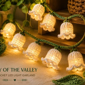 May include: A Lily of the Valley crochet LED light garland featuring white bell-shaped flowers attached to a green crocheted vine. The flowers are illuminated from within by warm glowing lights. The text reads LILY OF THE VALLEY CROCHET LED LIGHT GARLAND.