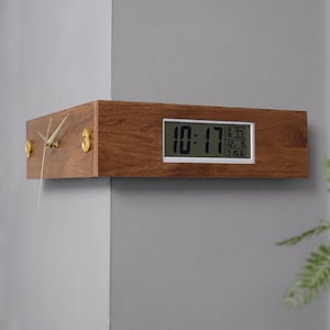 May include: A corner wall clock made of brown wood with a dual-sided design. One side features gold-colored hands and numerals, while the other side displays a digital screen showing the time 10:17, the date 12. 9., and a temperature of 15.6 degrees.