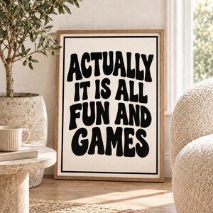 Può includere: Un quadro rettangolare incorniciato con sfondo color crema, bordo nero e una tipografia nera, audace e ondulata, che recita "ACTUALLY IT IS ALL FUN AND GAMES". La cornice è realizzata in legno chiaro con una finitura a venature naturali.