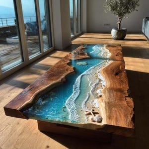 Puede incluir: Una mesa de centro rectangular con un tablero de madera de borde natural y una incrustación central de resina que imita una línea costera. La resina muestra tonos azules y turquesas con olas de espuma blanca, arena, una estrella de mar y conchas.