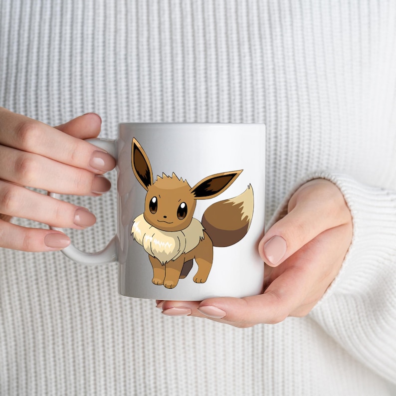 May include: A white ceramic mug featuring a graphic illustration of the brown and cream-colored Eevee character. The creature has large pointed ears, dark brown eyes, and a fluffy cream-colored collar around its neck with a bushy tail.