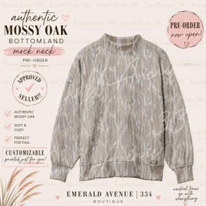 May include: A long-sleeve mock neck sweatshirt featuring an authentic Mossy Oak Bottomland camouflage pattern in shades of tan, brown, and grey. The garment has ribbed cuffs and a ribbed hem, with a small rectangular brand tag on the lower left side.