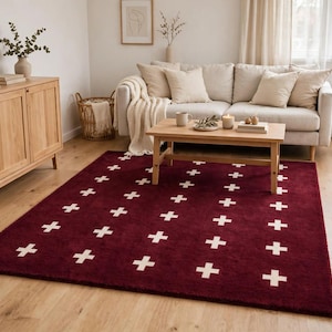 Puede incluir: Una alfombra rectangular que presenta un color base rojo burdeos intenso con un patrón repetitivo de pequeños símbolos de cruz en color blanco roto dispuestos en columnas verticales por toda la superficie del revestimiento del suelo.