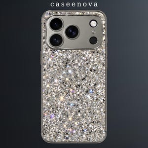 Puede incluir: Una funda para smartphone con un acabado de purpurina plateada densa y brillante que cubre el panel posterior. La funda incluye un borde transparente y un recorte rectangular para el módulo de cámara, con el texto caseenova impreso en la parte superior central.