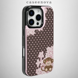 Puede incluir: Una funda de teléfono marrón con lunares blancos, detalles de encaje floral rosa claro y una ilustración de un mono. La funda tiene un marco negro alrededor de la lente de la cámara y el texto caseenova impreso en la parte superior.