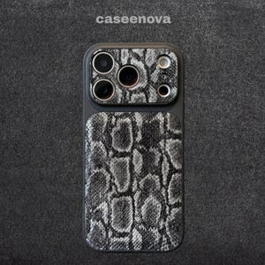 Pode incluir: Uma capa de smartphone com um padrão de pele de cobra em preto e branco na parte traseira e no módulo da câmera. A capa tem uma moldura preta e o texto caseenova está impresso em branco acima do dispositivo. O design cobre todo o painel traseiro.