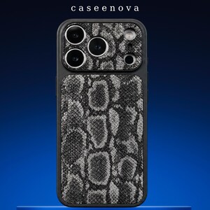 Puede incluir: Una funda de smartphone negra con un patrón texturizado de piel de serpiente gris y negra en el panel posterior y el área del módulo de cámara. El nombre de la marca caseenova está impreso en blanco sobre la funda. Tiene aberturas para tres lentes.