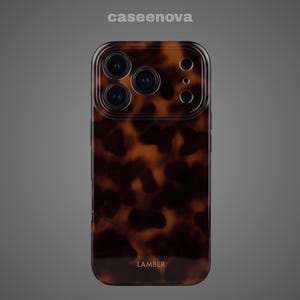 May include: A rectangular smartphone case featuring a brown and black tortoiseshell pattern. The case has a cutout for a triple-lens camera system and a flash. The word LAMBER is printed in small gold letters at the bottom center of the case.