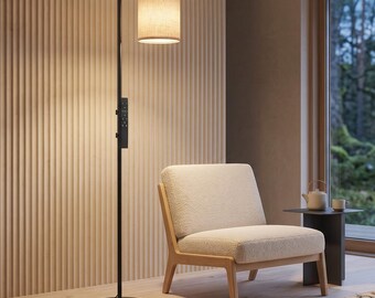 May include: A black floor lamp with a cylindrical beige fabric shade and a vertical control panel on the stem. The lamp stands on a circular base and emits a warm light, positioned next to a cream-colored upholstered chair with wooden legs.
