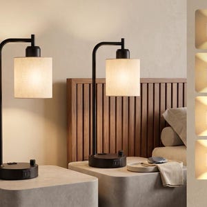 May include: A pair of black metal table lamps with cylindrical fabric shades. Each lamp features a curved arm, a circular base with a built-in USB port, and a rotary dimmer switch. The lamps emit a warm glow, shown in four distinct brightness levels.