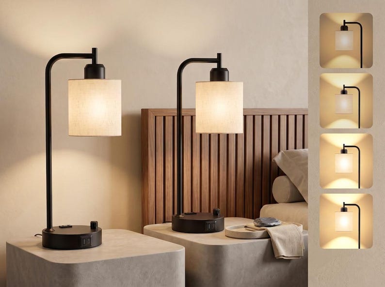 May include: A pair of black metal table lamps with cylindrical fabric shades. Each lamp features a curved arm, a circular base with a built-in USB port, and a rotary dimmer switch. The lamps emit a warm glow, shown in four distinct brightness levels.