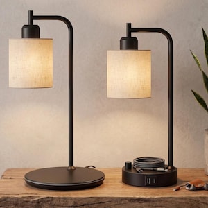May include: Two table lamps with matte black metal frames and cylindrical off-white fabric shades. The left lamp has a circular base, while the right lamp features a base with integrated USB ports, a rotary switch, and a coiled charging cable.
