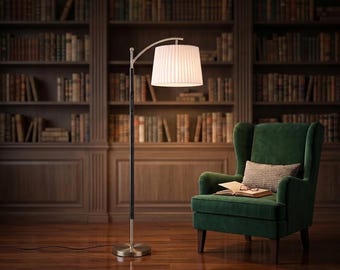 May include: A floor lamp with a brushed nickel finish, a slender black pole, and a white pleated drum shade. The lamp features an arched neck design, a circular base, and a power cord extending across the floor. It stands beside a green armchair.