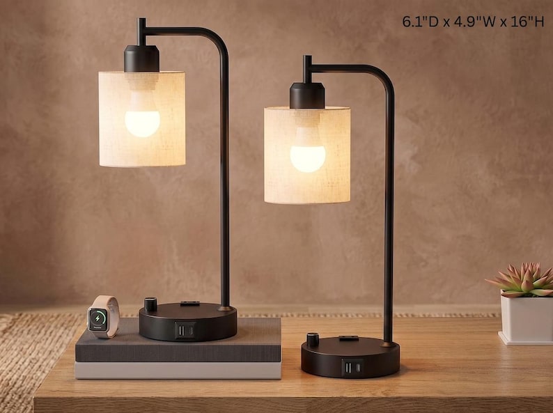 May include: Two black metal table lamps with cylindrical fabric shades and illuminated light bulbs. Each base features a rotary switch and two USB ports. The dimensions are 6.1 inches deep, 4.9 inches wide, and 16 inches high.