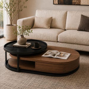 Puede incluir: Una mesa de centro de dos niveles con una base ovalada de madera con cajón y una bandeja superior circular de metal negro. La mesa sostiene un pequeño jarrón beige con vegetación, una taza oscura sobre un platillo y un libro abierto con páginas.