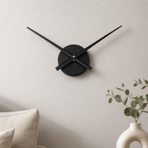 May include: A wall clock featuring a circular black centre hub and two long, slender black hands extending outwards. The clock lacks a traditional face, numbers, or markers, presenting a clean, geometric design with a matte black finish.