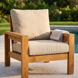May include: A wooden armchair with a natural light brown finish, featuring a square frame and thick, light beige cushions on the seat and backrest. A folded, textured light beige fabric throw is draped over the right armrest of the chair.