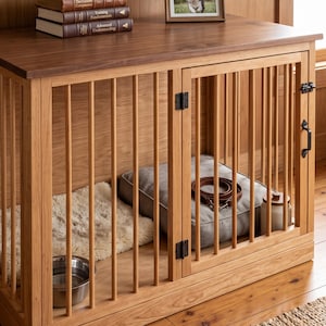 May include: A wooden dog crate with vertical slats and a hinged door featuring black metal hardware. Inside, a gray cushion, a brown leather leash, a cream-colored ceramic jar, a fluffy white rug, and a silver metal bowl are visible.