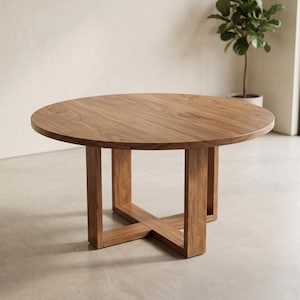 May include: A round dining table crafted from medium-brown wood with a visible grain pattern. The table features a flat circular top supported by a sturdy base consisting of four vertical legs connected by a central cross-shaped support structure.