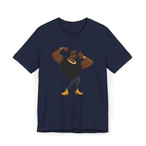 May include: A navy blue short-sleeve t-shirt featuring a graphic illustration of a muscular figure wearing a black t-shirt, dark pants, yellow boots, sunglasses, and a gold chain, posing with one arm flexed and the other hand near the face.