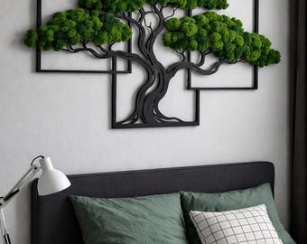 May include: A wall-mounted art piece featuring a black metal frame shaped like interconnected rectangles, containing a black silhouette of a tree with vibrant green preserved moss forming the foliage, displayed above a bed.