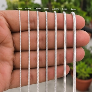 Puede incluir: Siete cadenas de serpiente plateadas de diferentes grosores dispuestas verticalmente, etiquetadas con medidas de 1,2 mm a 4 mm. Las cadenas presentan un patrón liso de estilo espiga entrelazado y un acabado metálico, mostradas en fila.