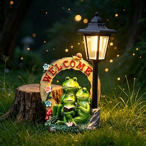 Può includere: Una lampada da giardino a energia solare con un palo nero fissato a un cartello circolare con la scritta WELCOME in lettere rosse. Tre rane verdi sono posizionate davanti al cartello, una delle quali legge un libro. Una piccola lumaca è in cima.