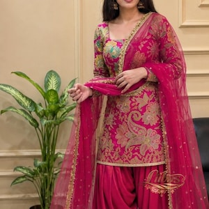 Könnte beinhalten: Ein leuchtend fuchsiafarbenes Salwar-Kameez-Set bestehend aus einer langärmeligen Tunika mit goldener und mehrfarbiger floraler Paisley-Stickerei, kombiniert mit einer passenden Plisseehose und einem transparenten Netz-Dupatta mit Goldpailletten und Bogenkante.