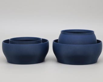 May include: Two sets of nested bowls in a matte dark blue finish. Each set consists of a larger outer bowl and a smaller inner bowl, both featuring a smooth, rounded silhouette with a wide base and a slightly tapered opening at the top.