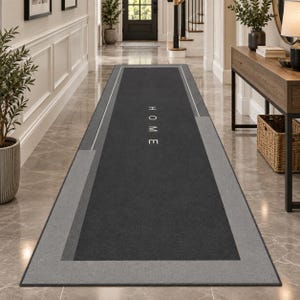 May include: A long rectangular runner rug featuring a dark charcoal gray center panel with the word HOME printed in white capital letters. The rug has a light gray border and geometric gray accents along the sides, creating a clean linear design.