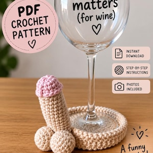 May include: A clear wine glass with the black text Size matters (for wine) and a heart symbol. Beside it sits a beige crochet coaster with an attached phallic-shaped crochet figure featuring a light pink top and a beige base.