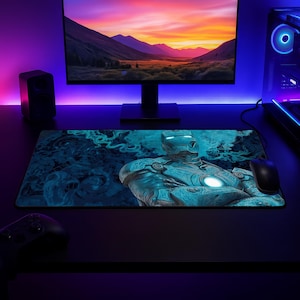 May include: A rectangular desk mat featuring a blue-toned graphic illustration of a robotic character with a glowing chest piece, surrounded by swirling smoke patterns. The mat is positioned on a dark surface beneath a computer monitor and mouse.