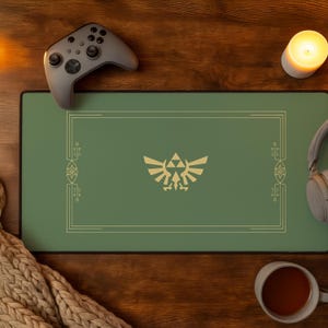 Peut inclure: Un tapis de bureau rectangulaire vert sauge arborant un emblème doré de la crête Hylienne au centre, entouré d'une fine bordure rectangulaire dorée avec des accents géométriques décoratifs sur les côtés gauche et droit du motif.