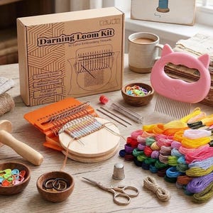 May include: A darning loom kit in a cardboard box labeled Darning Loom Kit, including an orange loom with a wooden disc, a pink cat-shaped comb, numerous colorful embroidery threads, metal needles, a thimble, scissors, and small bowls.