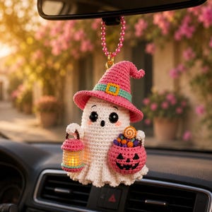 Peut inclure: Une breloque de voiture fantôme crochetée avec un chapeau de sorcière rose à bande turquoise, tenant une petite lanterne lumineuse et un seau citrouille rose rempli de bonbons colorés. L'ornement est suspendu par une chaîne de perles roses.