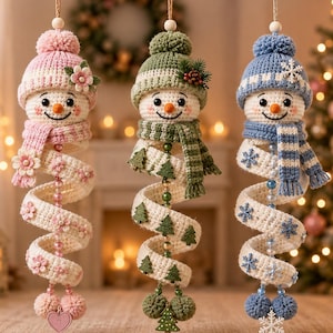 May include: Three hanging crochet snowman ornaments with spiral bodies. The left snowman wears a pink hat and scarf with flowers. The middle snowman has a green hat and scarf with pine trees. The right snowman features a blue hat and scarf with snowflakes.