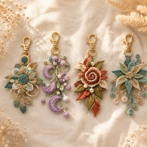 Puede incluir: Cuatro llaveros de ganchillo decorativos con cierres de langosta dorados. Los diseños incluyen una flor en color verde azulado y crema, una luna creciente morada con cuentas, un conjunto de hojas de otoño naranjas y verdes, y una flor en forma de estrella.