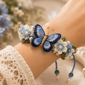 May include: A bracelet featuring a central blue and white crocheted butterfly with gold-toned antennae, flanked by crocheted blue and white flowers, green leaves, and white pearls. The bracelet has blue braided cords with small blue and gold beads.