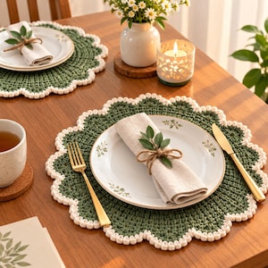 May include: A round, dark green crocheted placemat with a scalloped white border. The placemat holds a white ceramic plate with a botanical print, a beige linen napkin tied with twine and a green sprig, a gold fork, and a gold knife.