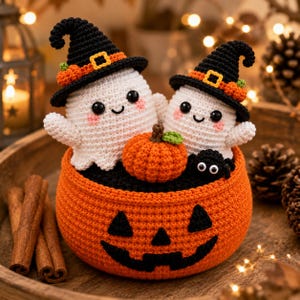 Può includere: Due fantasmi bianchi all'uncinetto che indossano cappelli da strega neri con fasce arancioni, seduti in un cesto a forma di zucca arancione all'uncinetto. Il cesto presenta una faccia di zucca nera. Una zucca arancione e un piccolo ragno nero sono all'interno.