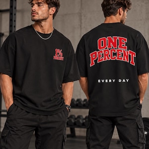 Könnte beinhalten: Ein schwarzes kurzärmeliges T-Shirt mit einer kleinen roten 1% PERCENT-Grafik auf der linken Brust. Auf der Rückseite befindet sich der große rote Schriftzug ONE PERCENT, der über dem weißen Text EVERY DAY in College-Schriftart steht.