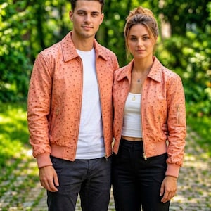 Può includere: Una giacca in pelle color pesca con un motivo testurizzato a pois, colletto classico, maniche lunghe con polsini a coste e chiusura frontale con zip. La giacca presenta finiture color oro, inclusa una piccola tasca con zip sulla manica sinistra.