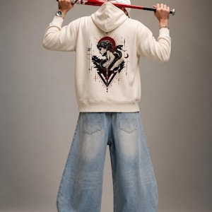 Peut inclure: Un sweat à capuche couleur crème avec une impression graphique au dos représentant un buste classique entrelacé d'un serpent, sur fond de motif circulaire rouge et de lignes géométriques. Le sweat est porté avec un jean bleu clair large.