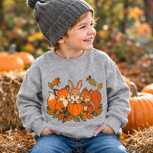 May include: A heather gray long-sleeve sweatshirt featuring a graphic print of a fox, a rabbit, and a squirrel sitting around a pumpkin, surrounded by autumn leaves. The sweatshirt has a crew neckline and ribbed cuffs at the sleeves and hem.