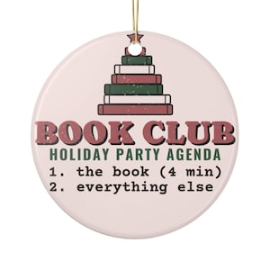 Può includere: Un ornamento rotondo in ceramica con un cordino dorato, raffigurante una pila di libri a forma di albero di Natale. Il testo recita: BOOK CLUB HOLIDAY PARTY AGENDA, 1. the book (4 min), 2. everything else. Lo sfondo è rosa chiaro.