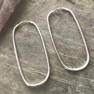 May include: A pair of silver oval hoop earrings. The earrings are large and have a smooth, polished finish.