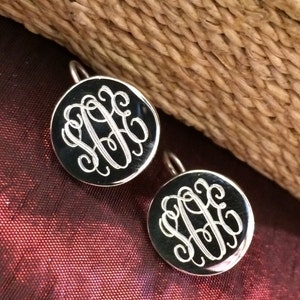 May include: A pair of silver earrings with a round, black disc featuring a monogrammed design.