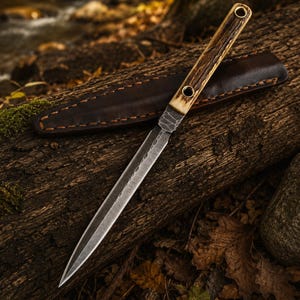 Könnte beinhalten: Ein feststehendes Messer mit einer langen, spitzen Stahlklinge, die nahe dem Griff eine gehämmerte Textur aufweist. Der Griff besteht aus strukturiertem braunem Geweih mit zwei Messingnieten. Eine dunkelbraune Lederscheide mit Nähten liegt bei.