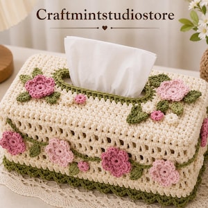 May include: A rectangular cream-colored crochet tissue box cover featuring a green vine border and decorative pink and light pink crocheted flowers with green leaves. The text Craftmintstudiostore is visible at the top of the image.