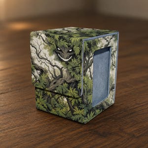 May include: A rectangular deck box featuring a detailed illustration of a forest creature with glowing white eyes and a wide grin hidden among green leaves and dark tree branches. The box has a textured exterior and a solid blue side panel.
